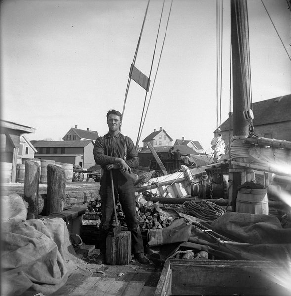 An Unidentified man chopping wood on the deck of a schooner